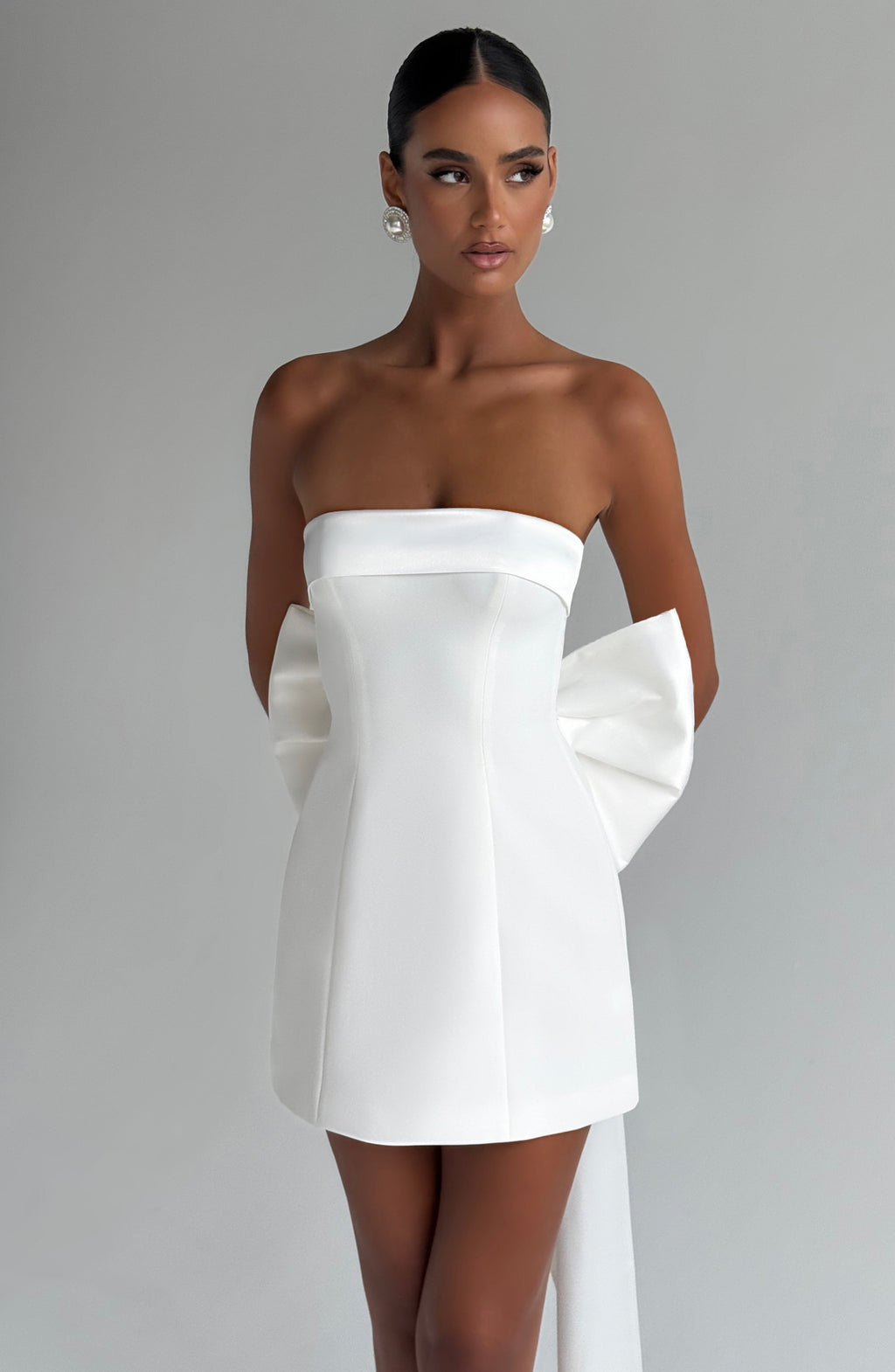 Woman wearing a white strapless A-line mini dress with an oversized back bow and long trailing tails