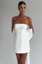 Woman wearing a white strapless A-line mini dress with an oversized back bow and long trailing tails