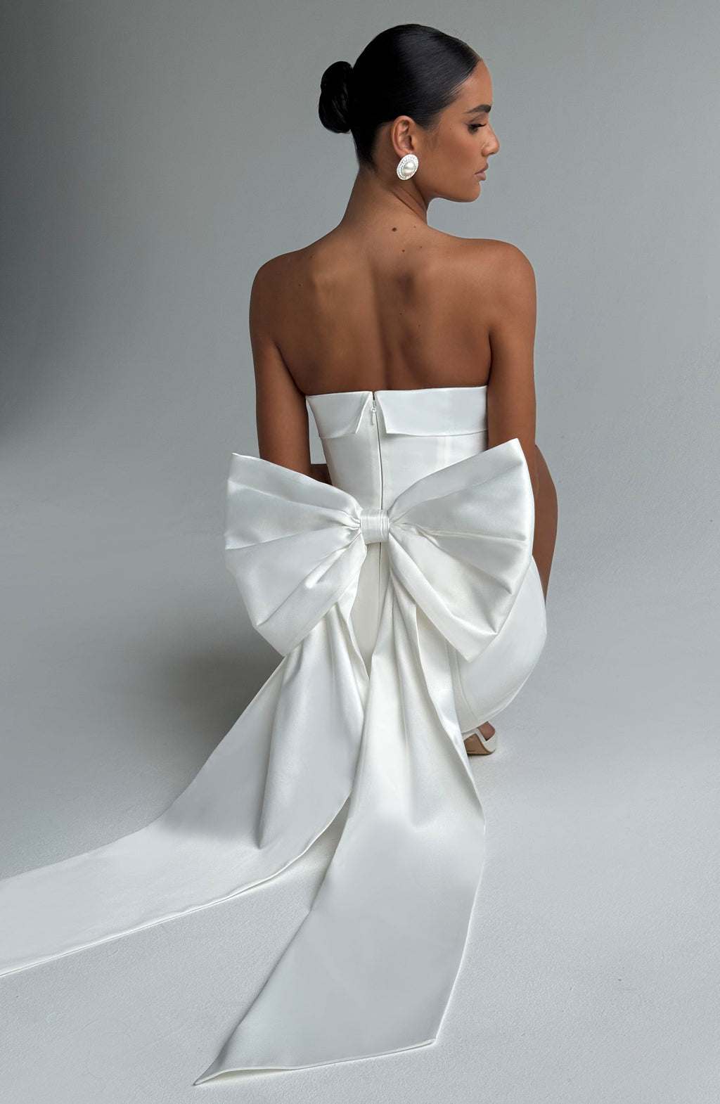 Woman wearing a white strapless A-line mini dress with an oversized back bow and long trailing tails - view 2