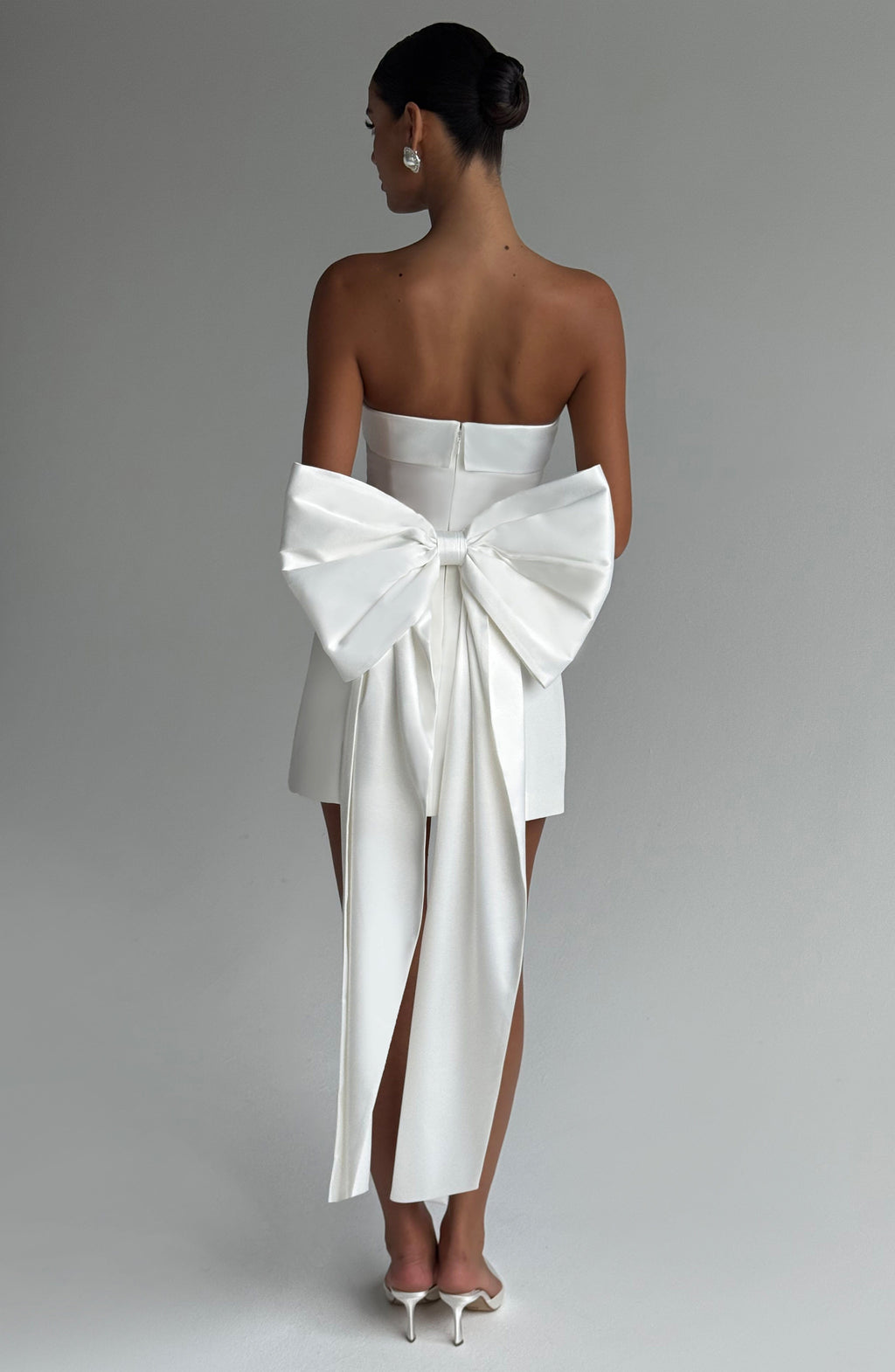 Woman wearing a white strapless A-line mini dress with an oversized back bow and long trailing tails - view 3