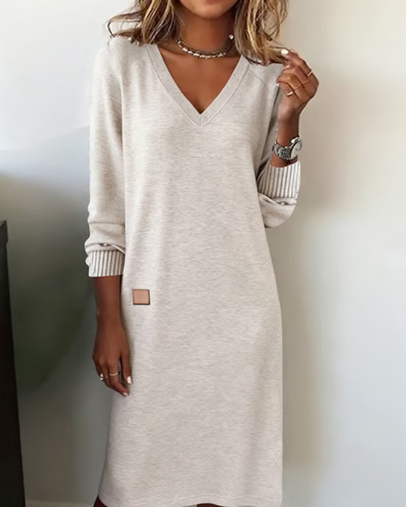 Woman wearing a V-neck long sleeve midi sweater dress with ribbed cuffs and a small patch detail