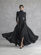 Woman in a black pleated turtleneck maxi dress with long sleeves and front slit
