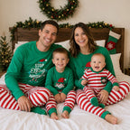 Family in matching green elf graphic tops and red and white striped Christmas pajama pants
