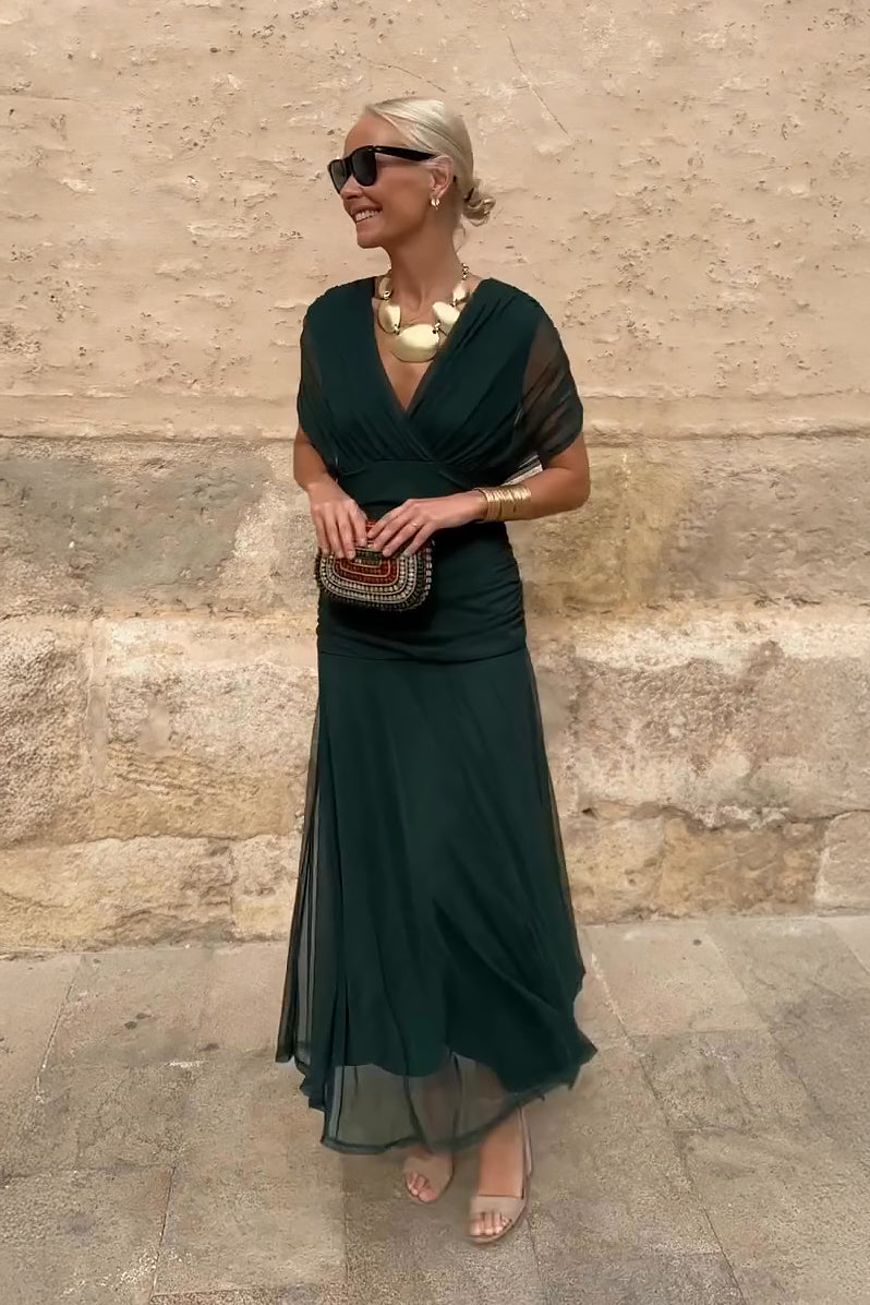 Woman wearing an emerald green mesh maxi dress with draped V-neck and ruched waist
