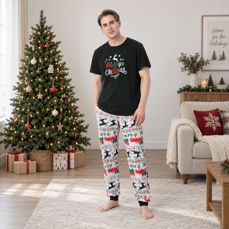 Family wearing matching black Merry Christmas tees and reindeer print jogger pajamas by a Christmas tree - view 2