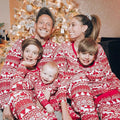 Family wearing matching red and white reindeer print Christmas pajamas by the tree