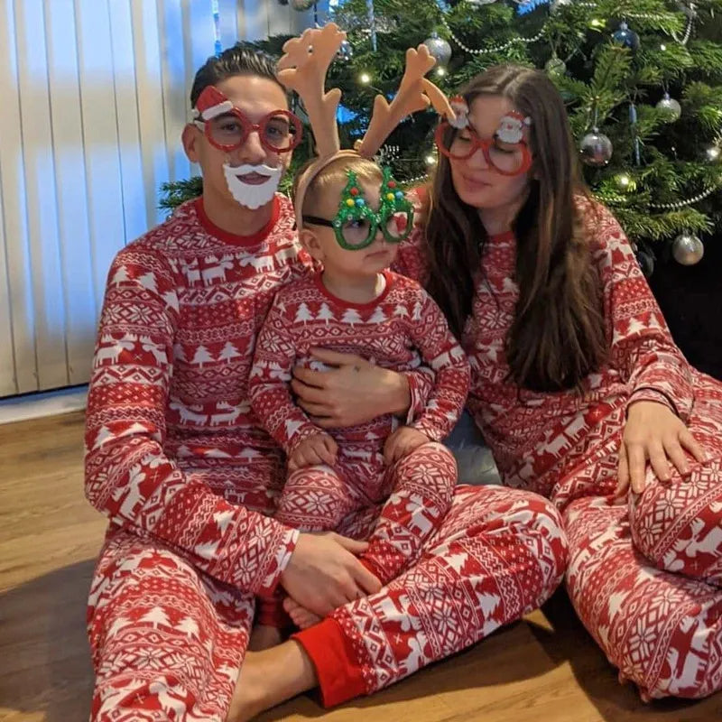 Family wearing matching red and white reindeer print Christmas pajamas by the tree - view 2